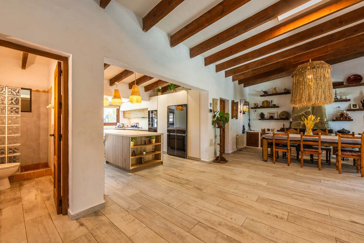 Salón cocina rústica con vigas de madera, isla y comedor con lámpara de fibra natural
