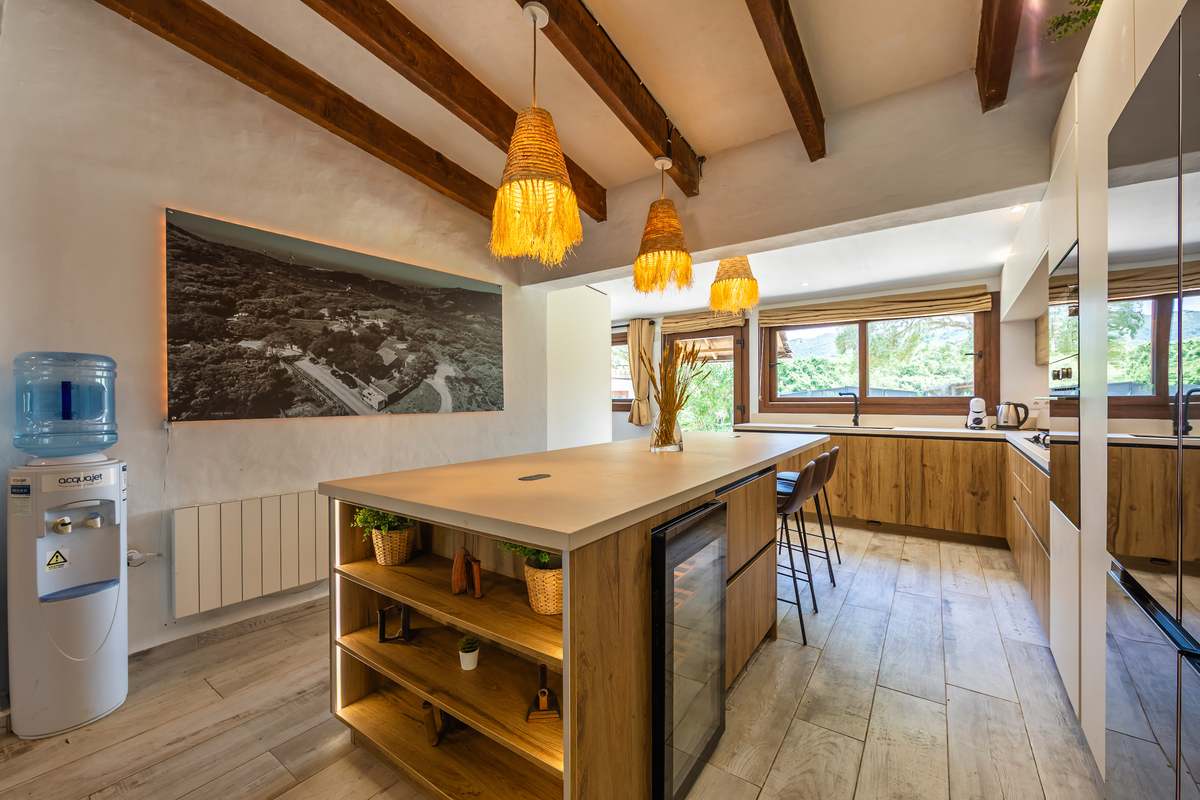 Cocina rústica con isla de madera, lámparas de mimbre y vigas de madera vistas