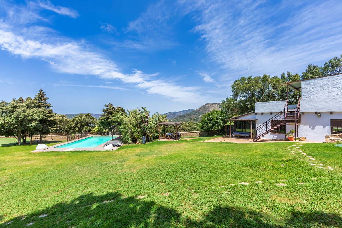 Jardín amplio con piscina, césped verde y vistas a las montañas de Tarifa