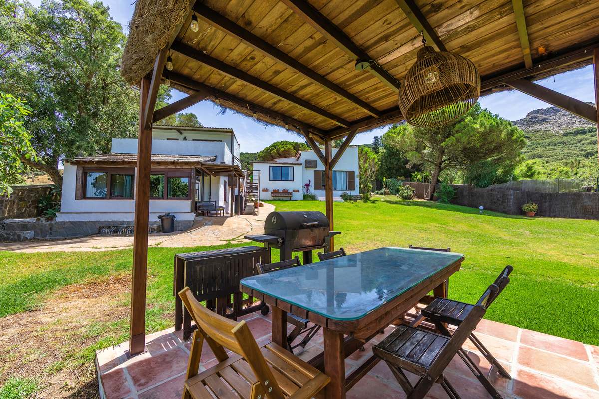 Porche con techo de paja, mesa de cristal y barbacoa junto al jardín con vistas a la montaña en Tarifa