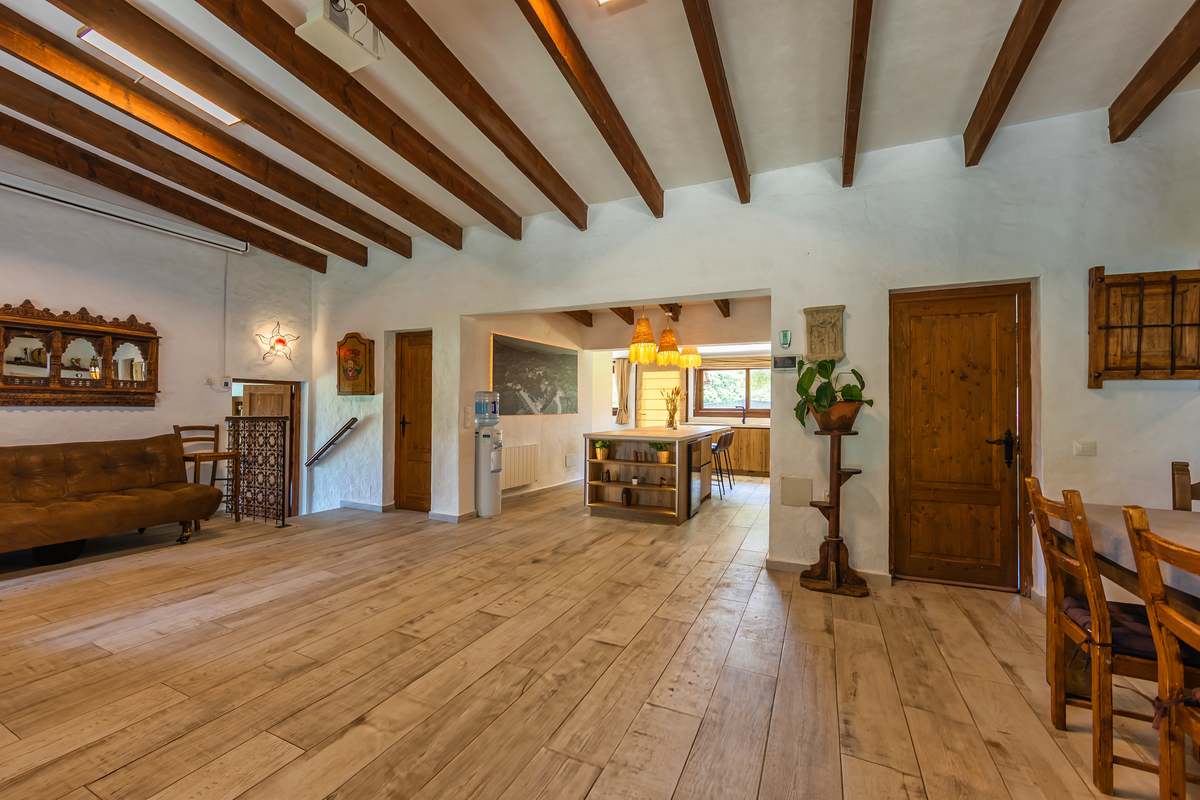 Salón amplio con techo de vigas de madera, suelo de parquet y acceso a cocina rústica
