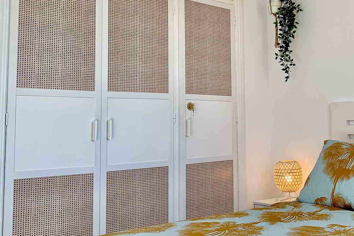 Armario empotrado en el dormitorio de Los Lances 2, con diseño blanco y paneles de mimbre, decorado con detalles naturales.