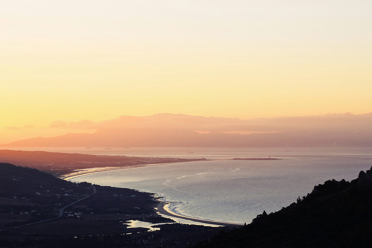 Vista panorámica del atardecer en Tarifa mostrando la unión del Mediterráneo y el Atlántico, con las montañas de África en el horizonte.
