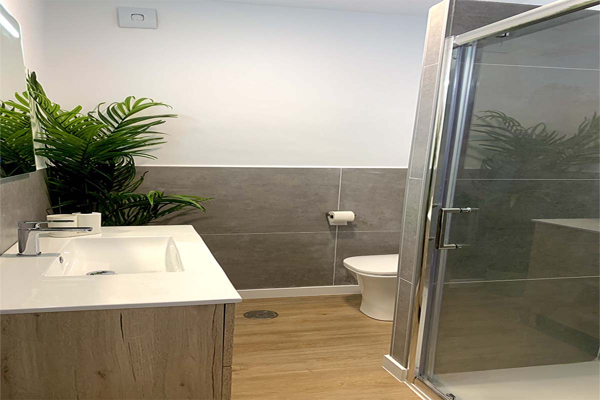 Baño moderno con plato de ducha, lavabo de madera y planta decorativa.