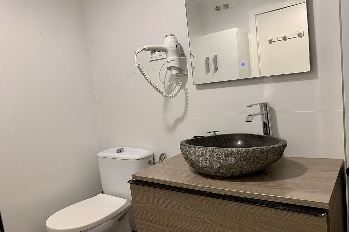Baño moderno con lavabo de piedra y espejo amplio.