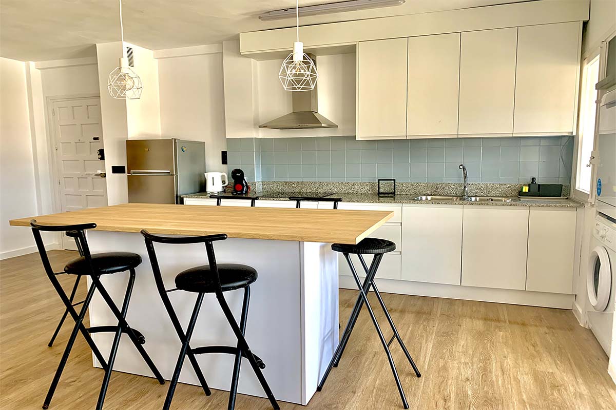 Cocina moderna con isla central, taburetes y electrodomésticos integrados.