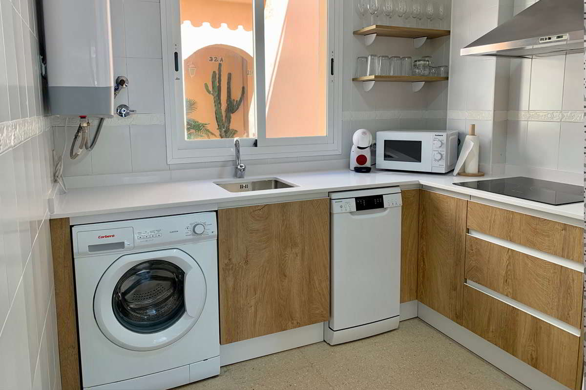 Cocina moderna con muebles de madera, electrodomésticos y ventana luminosa.