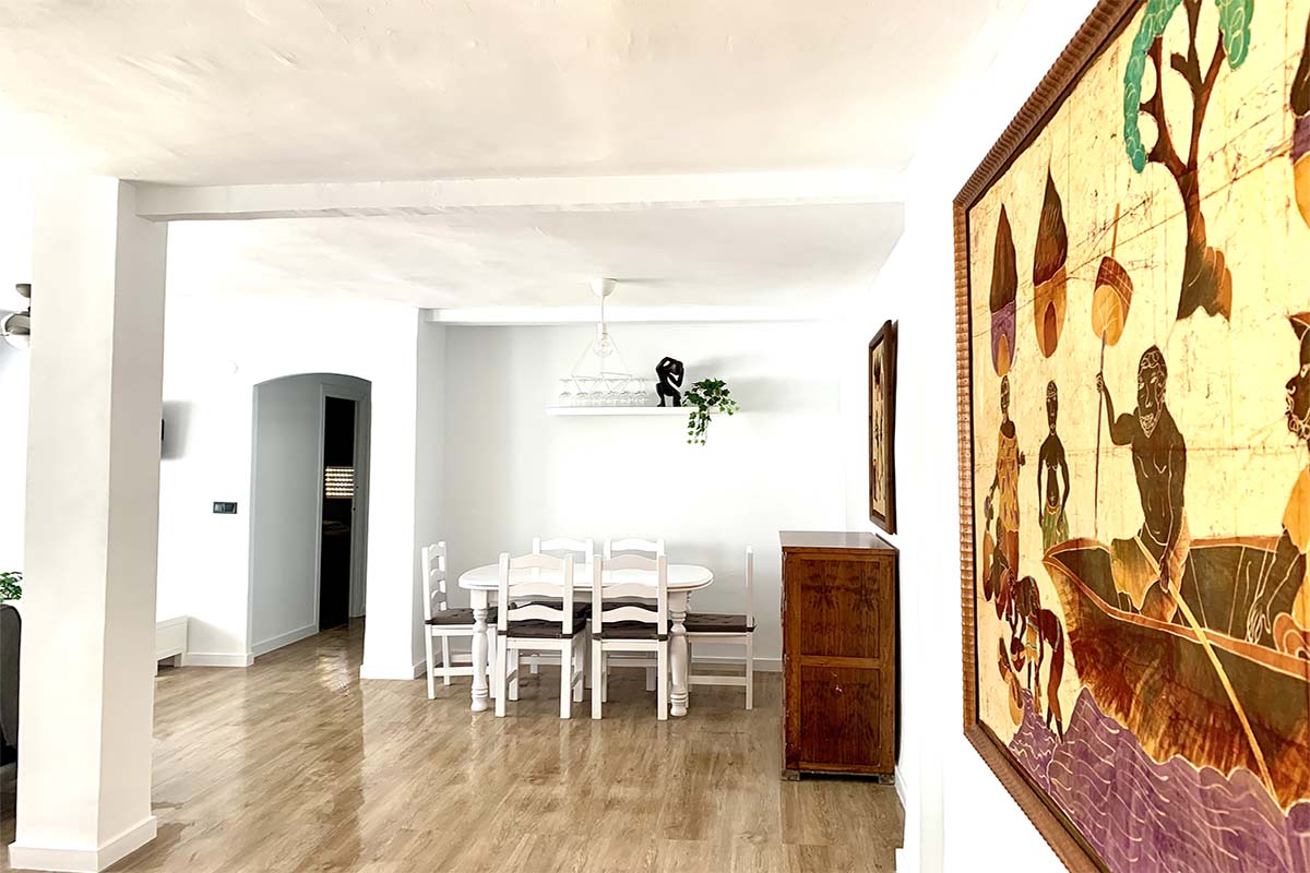 Comedor amplio con mesa blanca, sillas de madera y decoración artística.