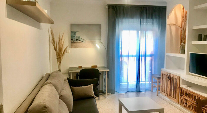 Salón del apartamento Callao con sofá, escritorio y decoración en tonos neutros con detalles cálidos.