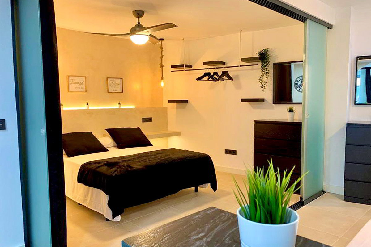 Dormitorio con cama doble, lámparas colgantes y estantes abiertos en la pared blanca.