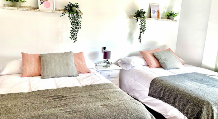 Dormitorio del Apartamento Tinto con dos camas individuales, decoración en tonos suaves y detalles vegetales.