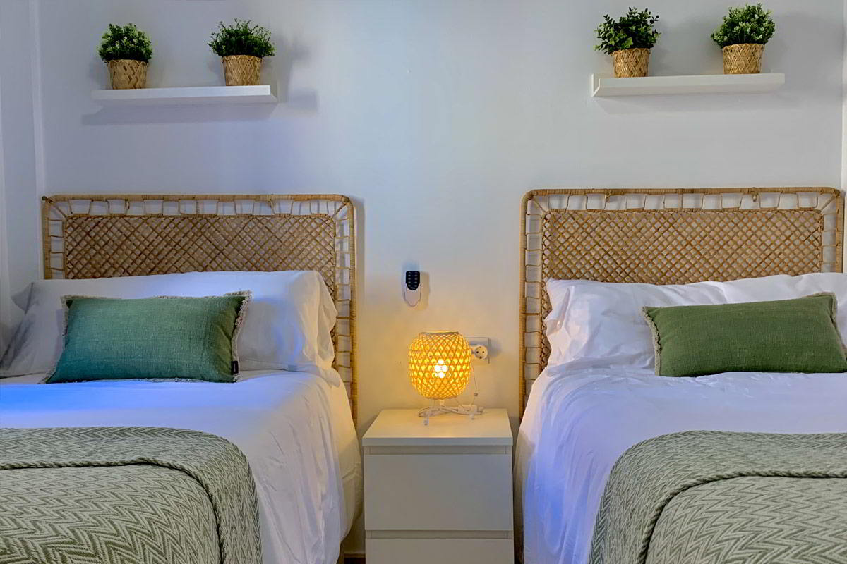 Dormitorio doble en Los Lances 2 con cabeceros de mimbre, ropa de cama en tonos verdes y detalles decorativos naturales.