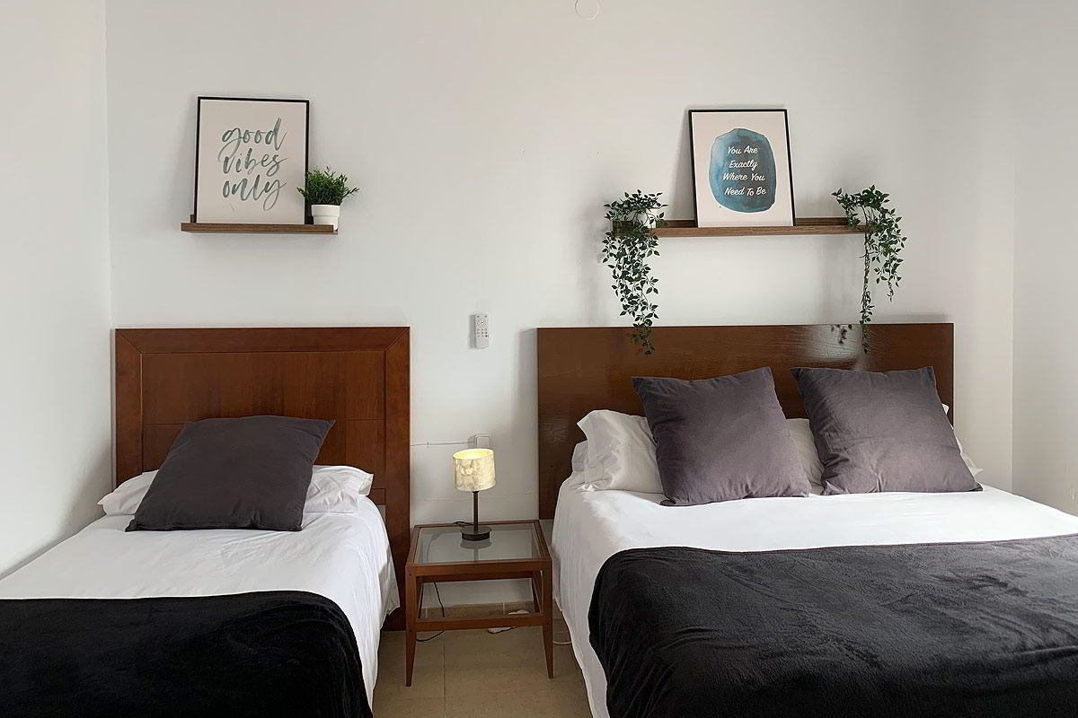 Dormitorio con camas individuales en el apartamento Freedom, decorado con cabeceros de madera y estanterías con plantas