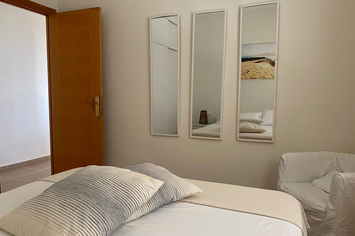 Dormitorio con cama doble, cojines y tres espejos verticales en la pared.