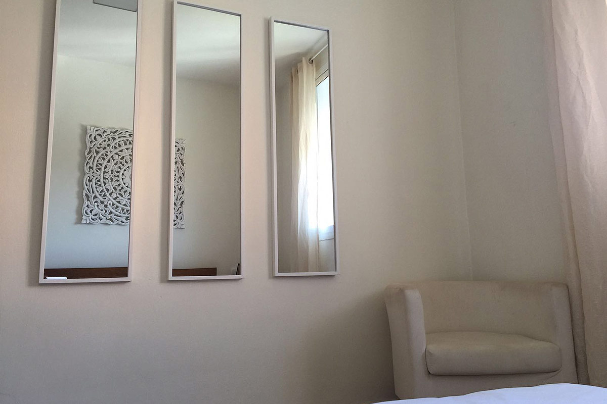 Dormitorio con sillón blanco y tres espejos decorativos en la pared.