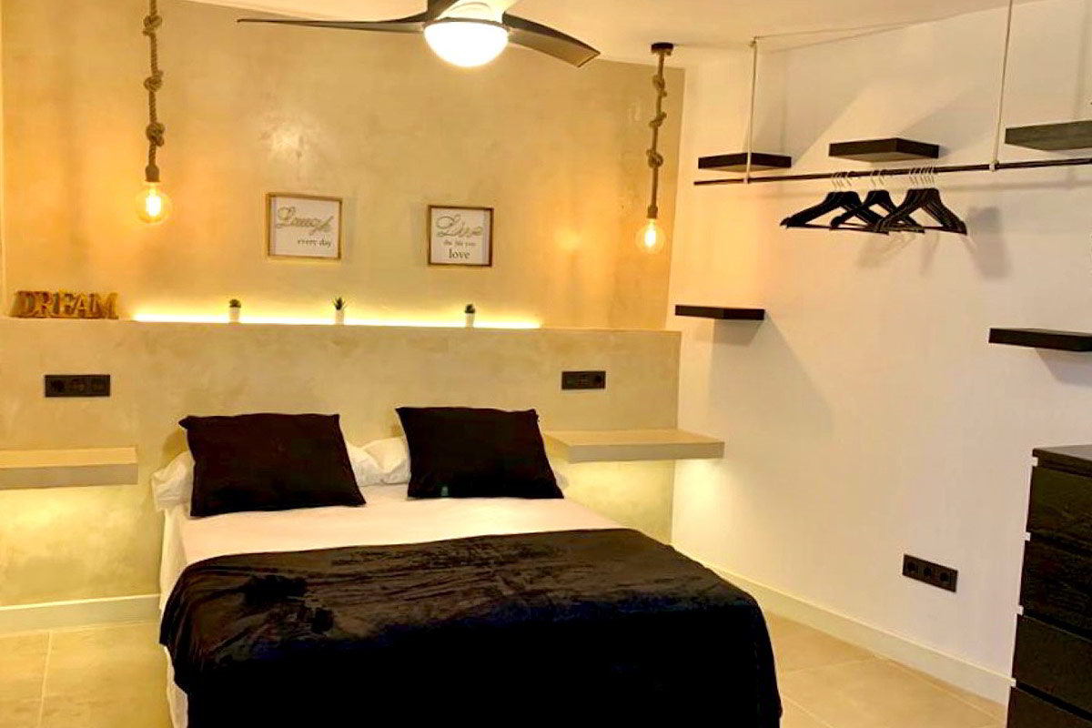 Vista del dormitorio principal con cama doble, estantes abiertos y detalles decorativos.