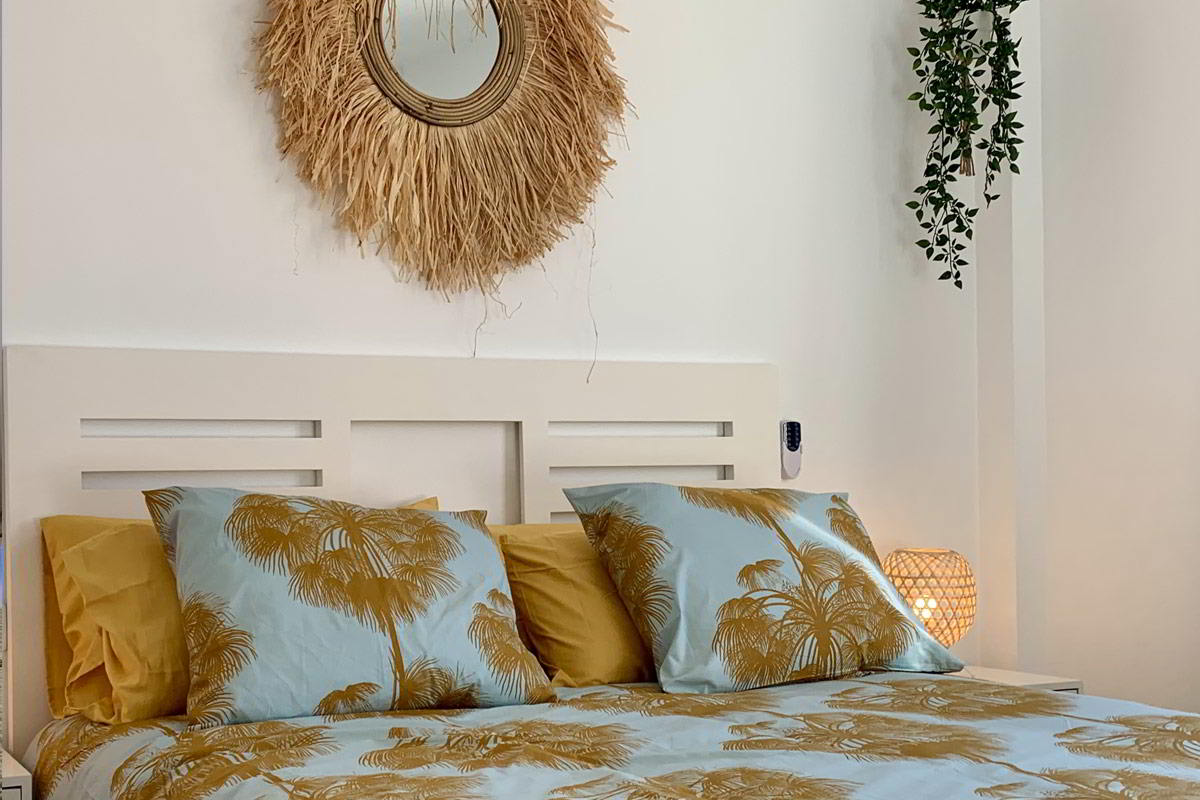 Dormitorio principal en Los Lances 2 con cama doble, ropa de cama estampada y decoración natural con espejo de fibras.