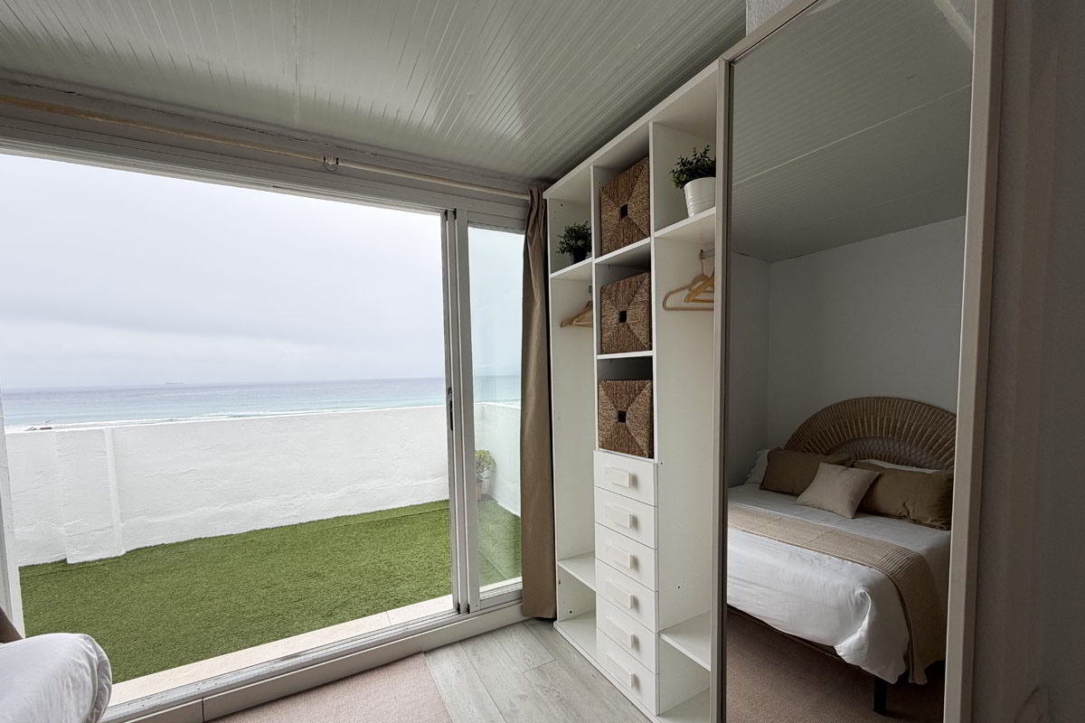 Dormitorio con armario abierto y salida a terraza con vistas al mar en apartamento Infinity.