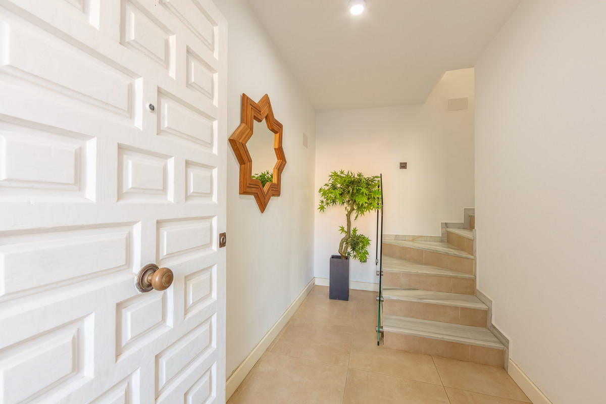 Entrada luminosa con puerta blanca, escaleras interiores y decoración sencilla.