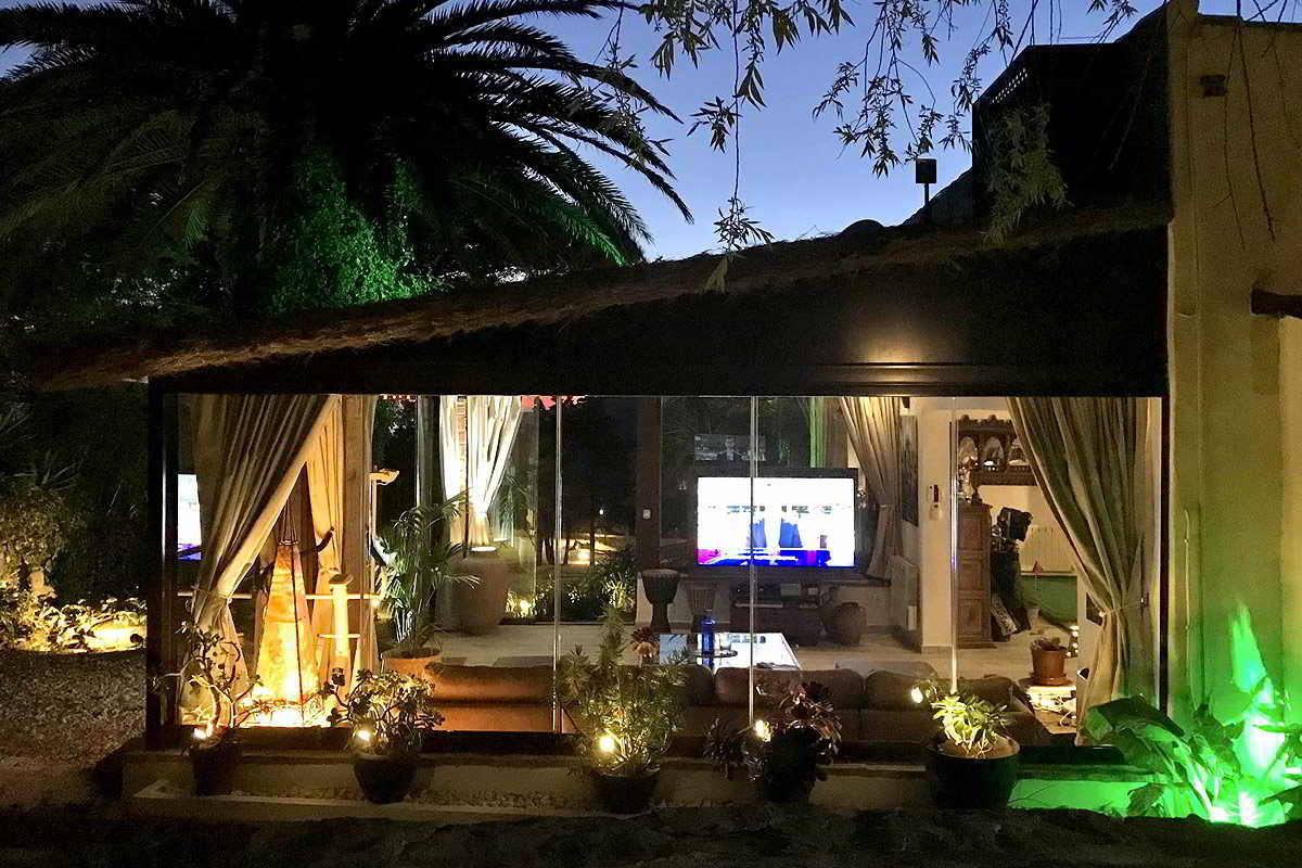Vista nocturna del exterior del chalet La Ahumada, mostrando el interior iluminado con detalles de jardinería y una atmósfera serena