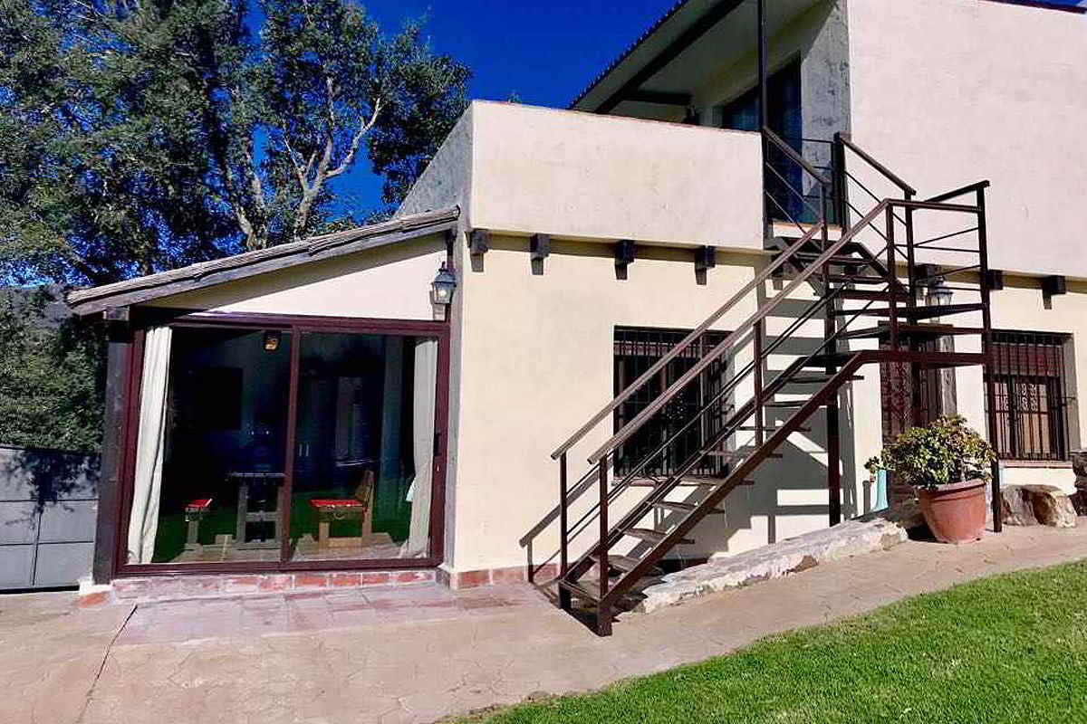 Fachada principal del chalet La Ahumada durante el día, destacando su diseño rústico y entorno natural con césped y vegetación.