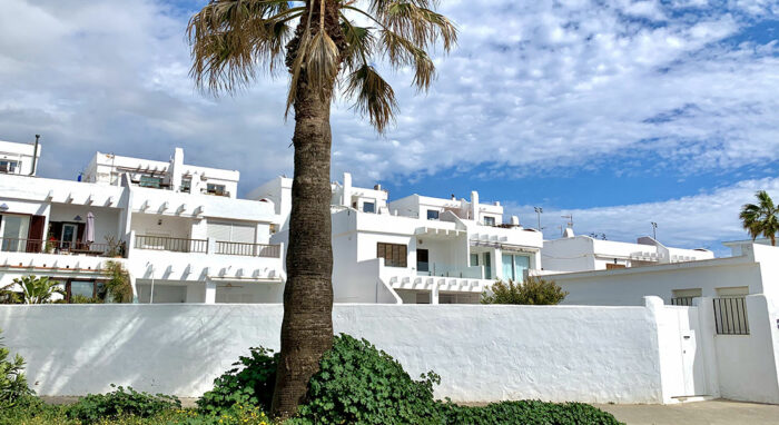 Fachada blanca de estilo mediterráneo en la Urbanización Las Cañas con palmera en primer plano y cielo despejado.