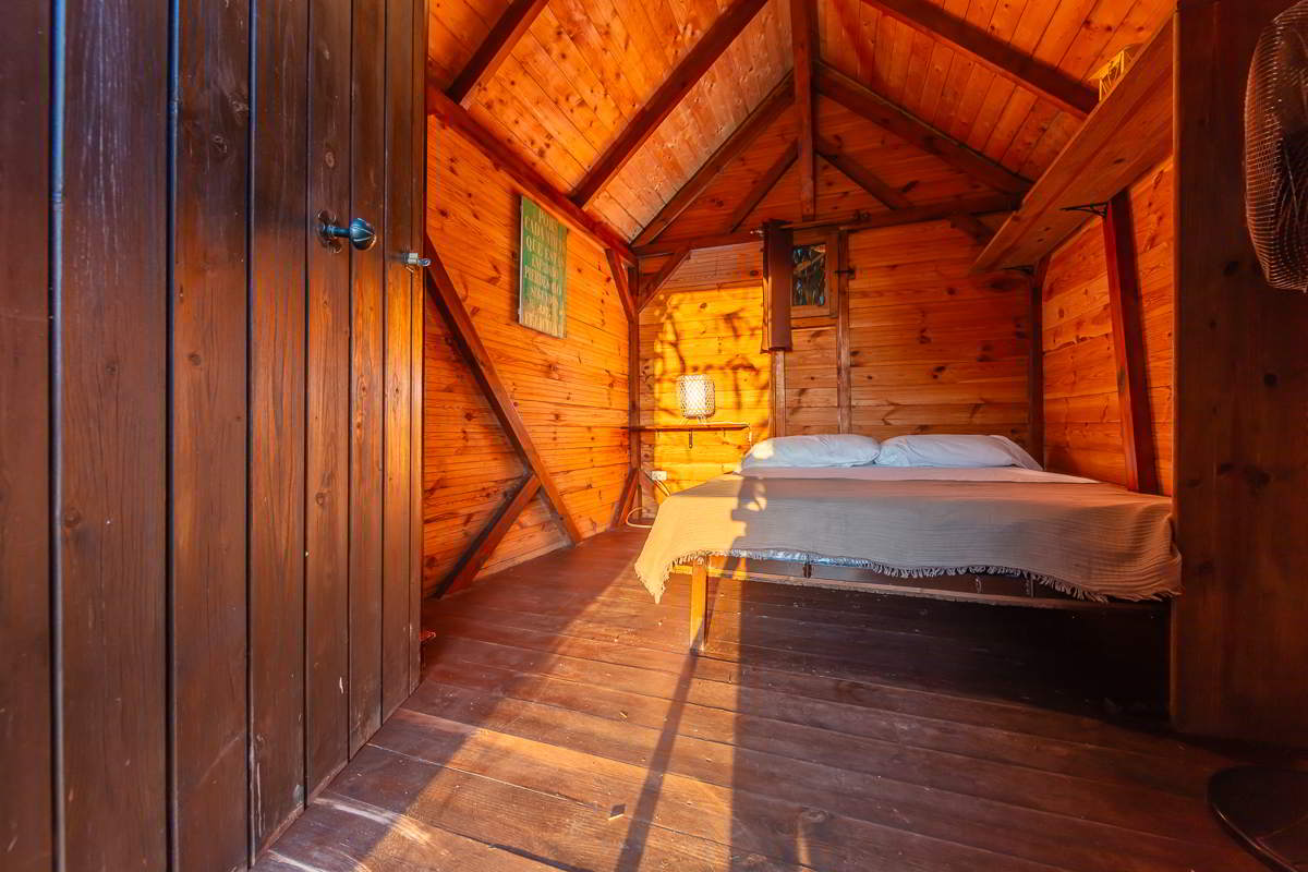 Interior de la cabaña del Chalet La Ahumada con paredes y techo de madera, cama doble y luz cálida de atardecer entrando por la puerta.