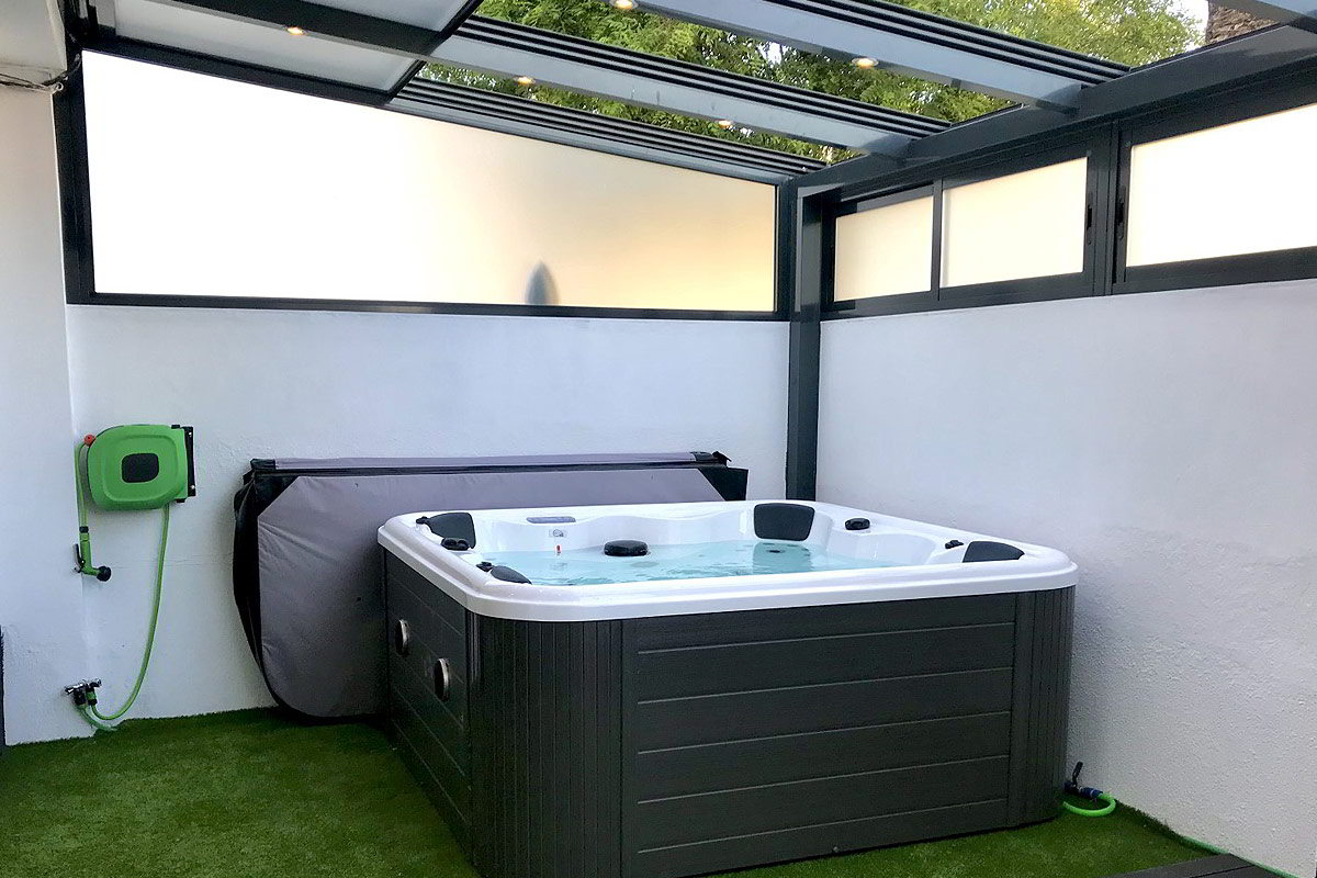Jacuzzi moderno bajo techo transparente en terraza privada con paredes blancas.