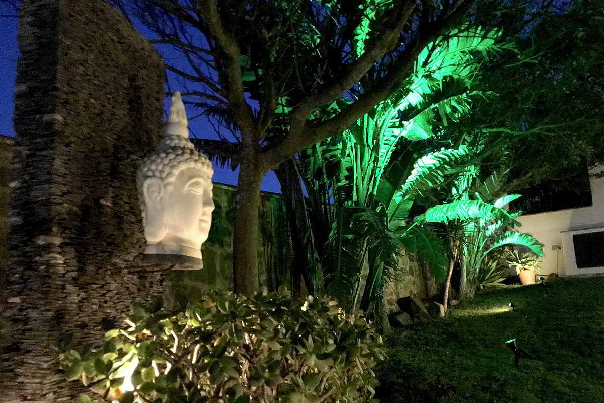 Jardín iluminado del chalet La Ahumada al anochecer, con decoración de esculturas y vegetación exótica.