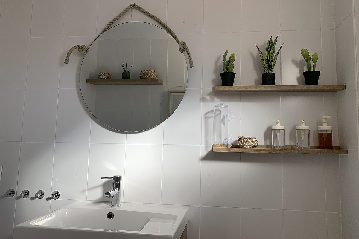 Detalle del lavabo en el baño de Los Lances 2 con espejo redondo y estanterías decoradas con plantas y accesorios.