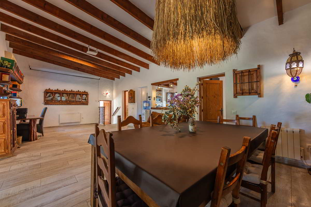 Espacioso comedor interior del Chalet La Ahumada, con mesa de madera, sillas rústicas, lámpara de fibras naturales y vigas vistas en el techo.