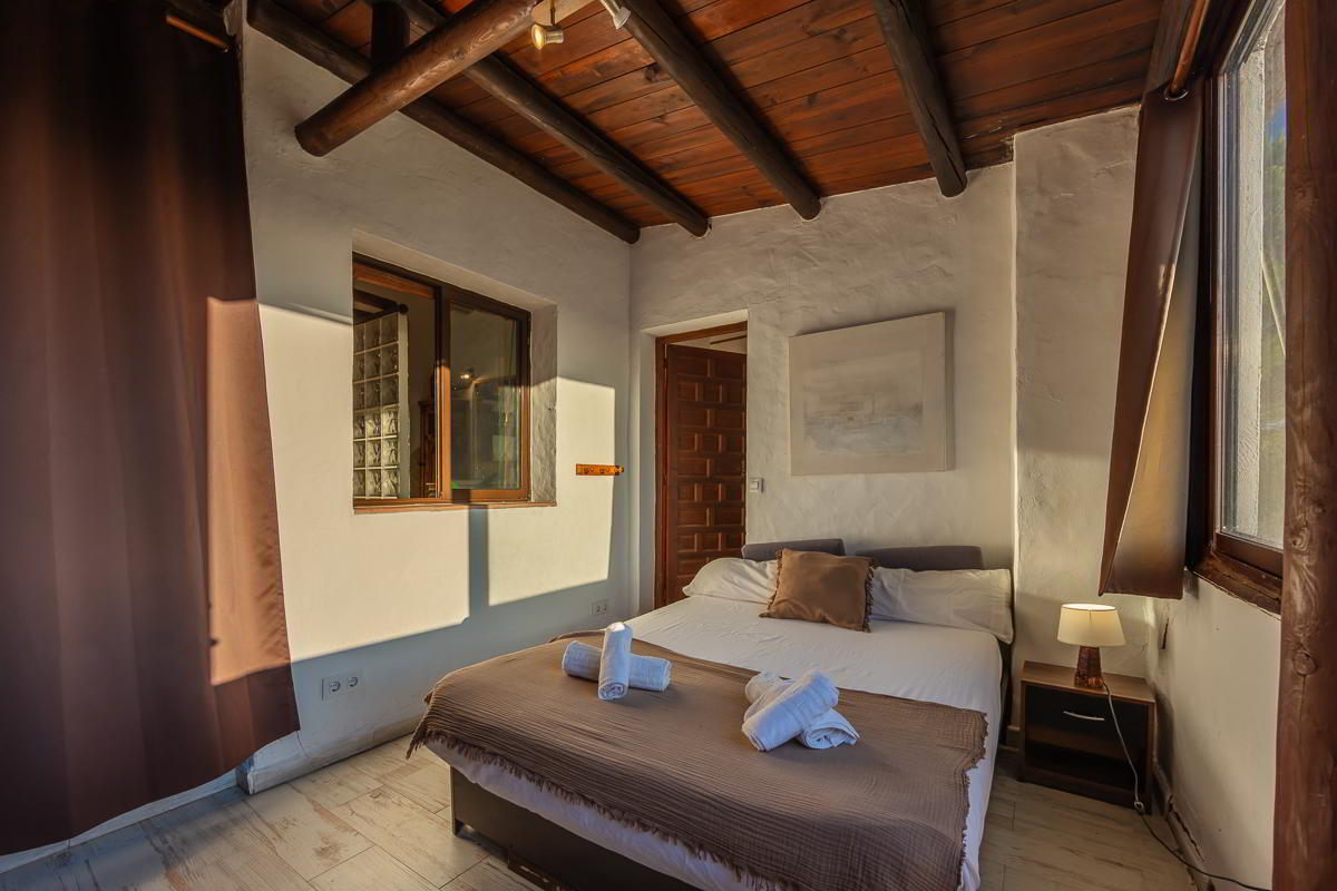 Dormitorio rústico del chalet La Ahumada con cama doble, techo de vigas de madera y luz cálida de atardecer.
