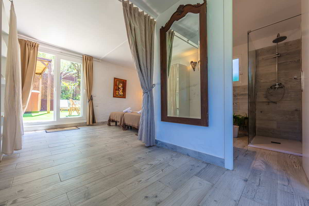 Habitación con cama doble, acceso directo al jardín, cortinas divisorias, espejo vintage de madera y baño con ducha de estilo moderno con revestimiento en imitación madera.