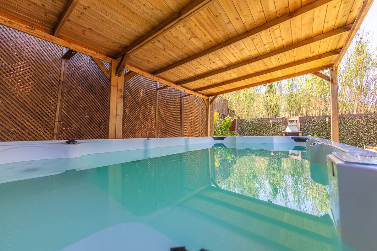 Detalle del jacuzzi cubierto con estructura de madera en Villa Verde, rodeado de setos y vegetación, con agua turquesa y ambiente relajante.
