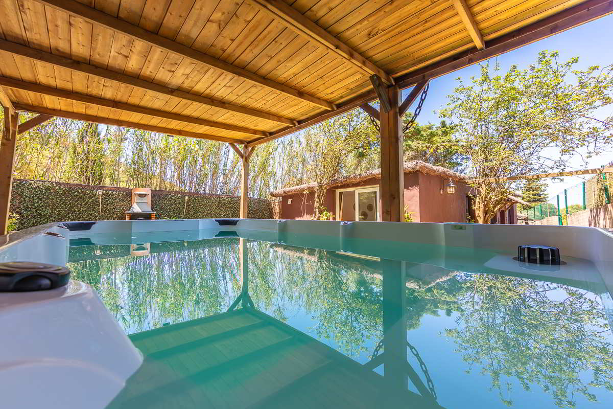 Jacuzzi exterior cubierto en Villa Verde con reflejos del cielo y la vegetación sobre el agua turquesa, junto a la fachada de la casa y un entorno de naturaleza.