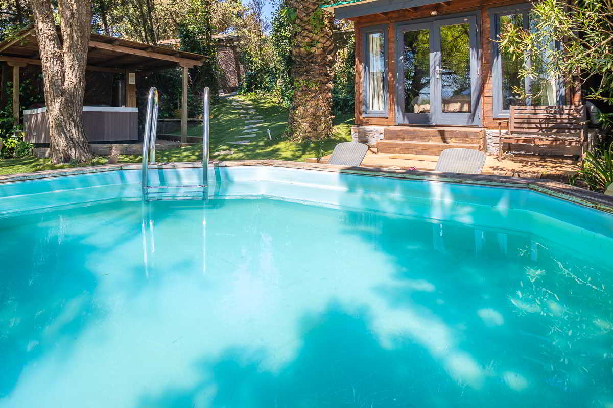 Piscina privada de la casa Nepal en Villas La Ahumada, rodeada de árboles y vegetación exuberante, con jacuzzi bajo pérgola de madera, tumbonas y acceso directo a la cabaña de estilo rústico