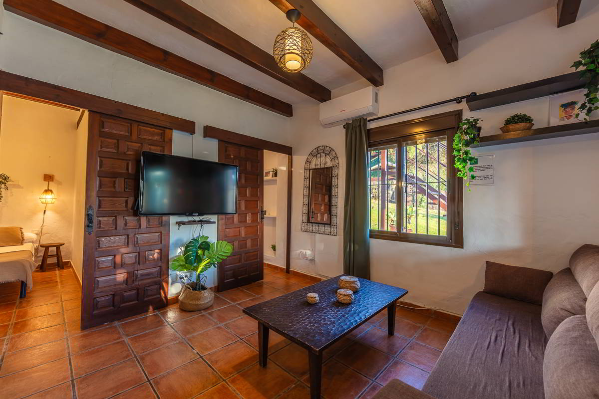 Salón de Villa Paraíso en Villas La Ahumada, Tarifa, con sofá marrón, mesa de centro oscura, televisor de pantalla plana y detalles decorativos cálidos.