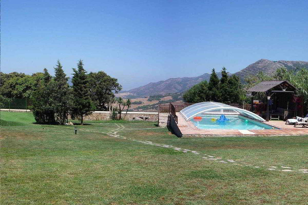 Piscina climatizada en el jardín del chalet La Ahumada, rodeada de césped, árboles y vistas al Parque Natural de Los Alcornocales.