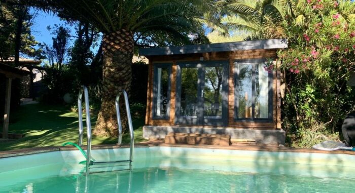 Piscina en la Villa Nepal rodeada de vegetación tropical con una caseta de madera al fondo.