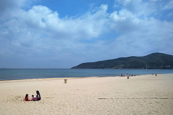 Playa de Getares con arena dorada, aguas tranquilas y colinas verdes al fondo.