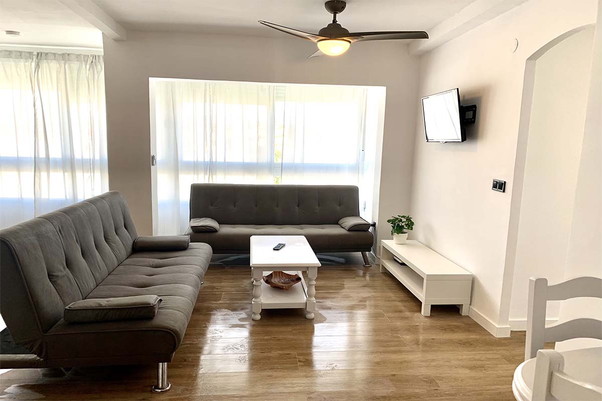 Sala de estar con sofás grises, mesa de centro y televisor en la pared.