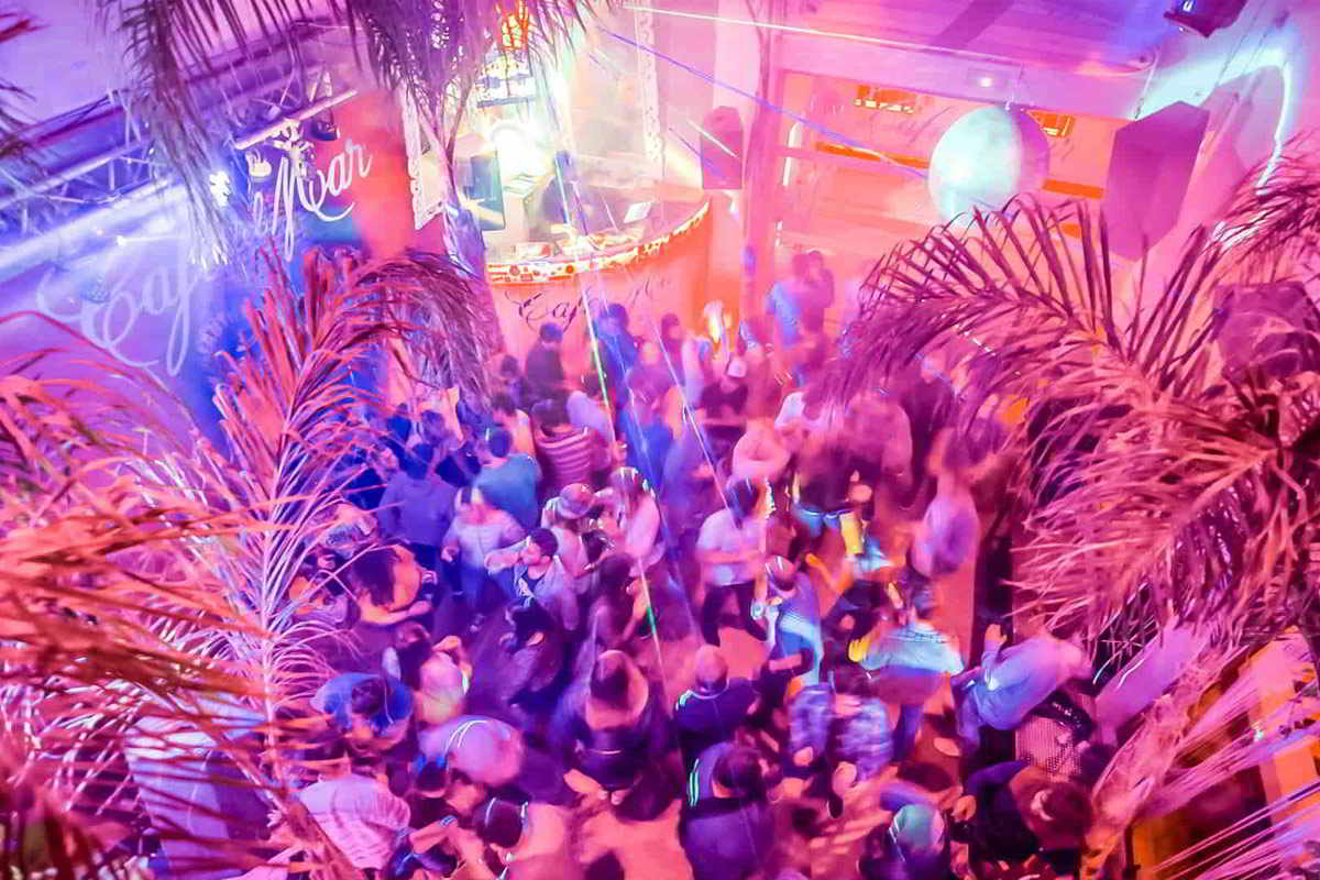 Vista aérea del interior de la discoteca Café del Mar en Tarifa, con luces vibrantes, palmeras decorativas y una multitud disfrutando del ambiente nocturno.