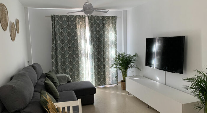 Salón del apartamento Los Lances 2 con sofá chaise longue, televisor y decoración moderna en tonos neutros.