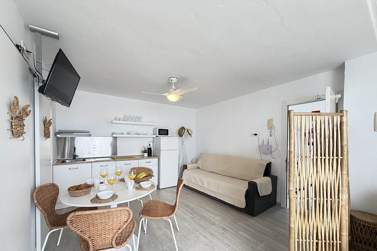 Salón con cocina abierta, comedor y sofá cama en apartamento Infinity en Tarifa.