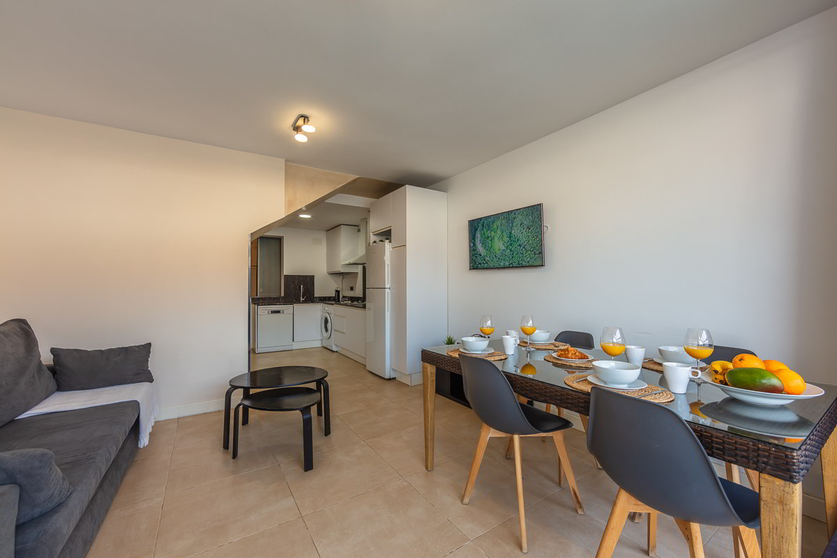 Salón comedor con cocina abierta del apartamento Las Gaviotas 9B en Tarifa equipado con mesa para cuatro personas y zona de estar.