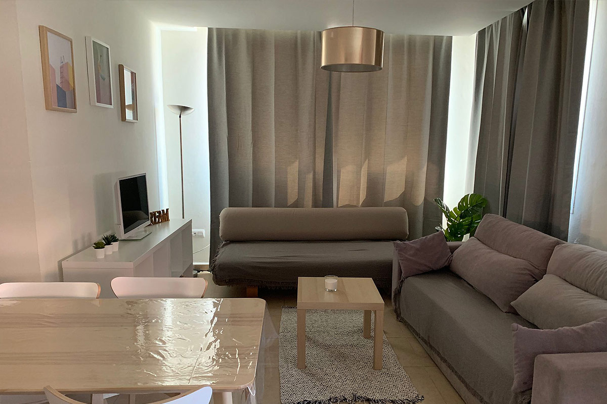 Salón con mesa de comedor, sofás grises y grandes cortinas.