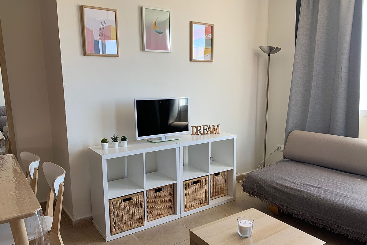 Salón con estantería blanca, sofá gris y cuadros en la pared.