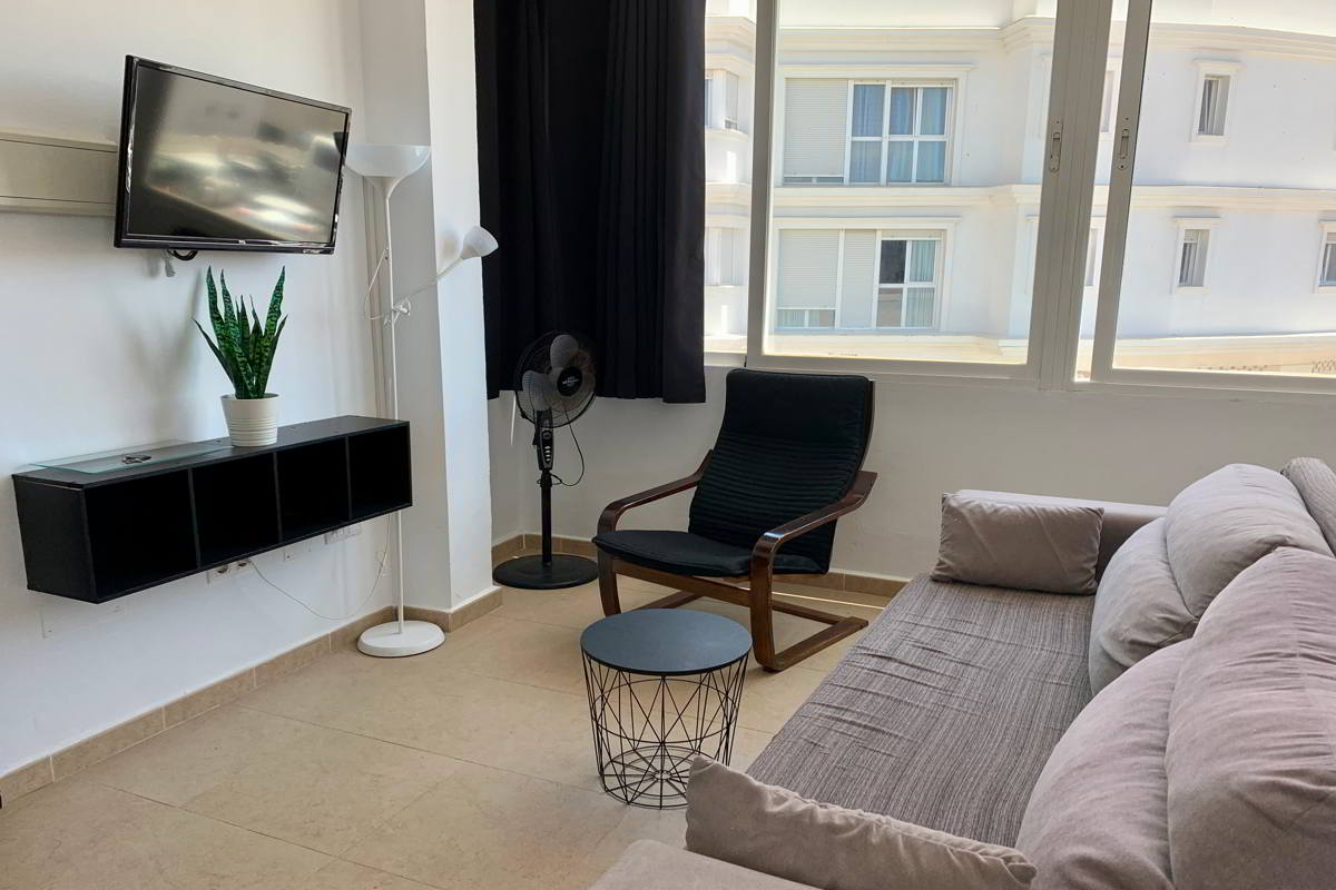 Salón con sofá amplio, silla moderna, televisor y gran ventana luminosa.