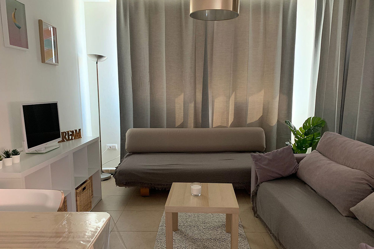 Salón con estantería blanca, sofá gris y cuadros en la pared.