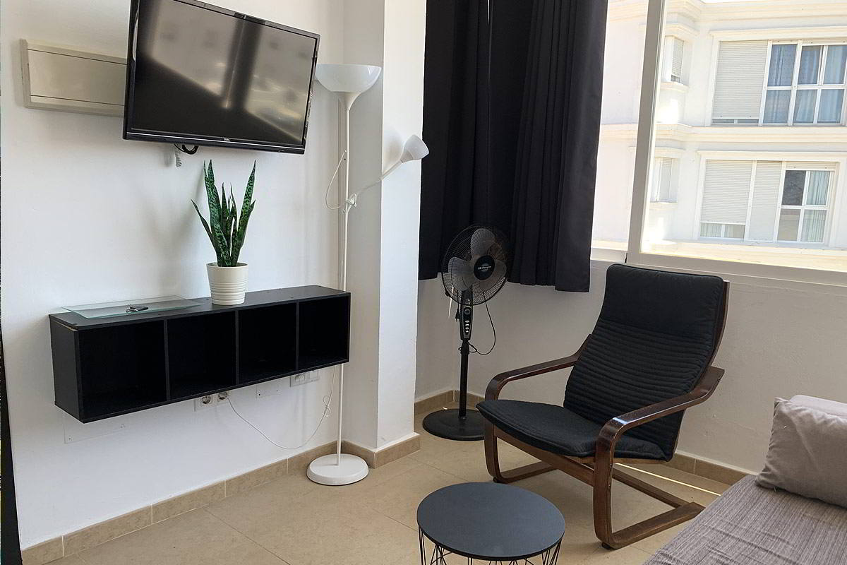 Salón con televisor, silla cómoda, ventilador y ventana luminosa.